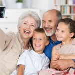 Grandparents and grandchildren sitting together in a close group on a sofa laughing and doing a self portrait with a hand held camera on a mobile phone